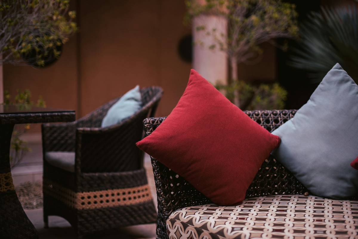 geometric garden pillows for patio decor arranged on a white wicker sectional with navy throw blanket and potted boxwoods
