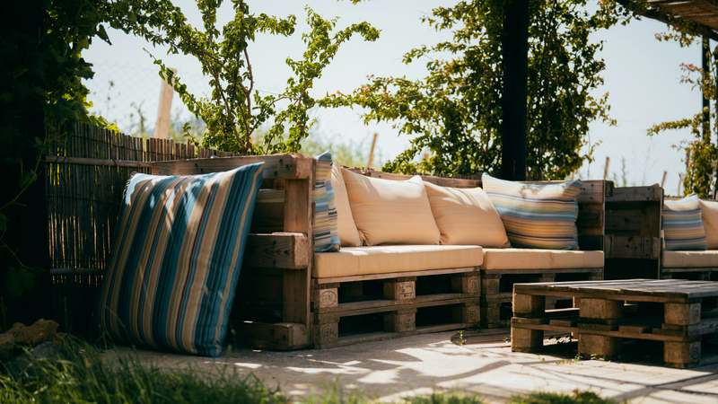 Stylish beige-and-navy outdoor pillows arranged on a teak sofa with potted herbs and soft ambient lighting
